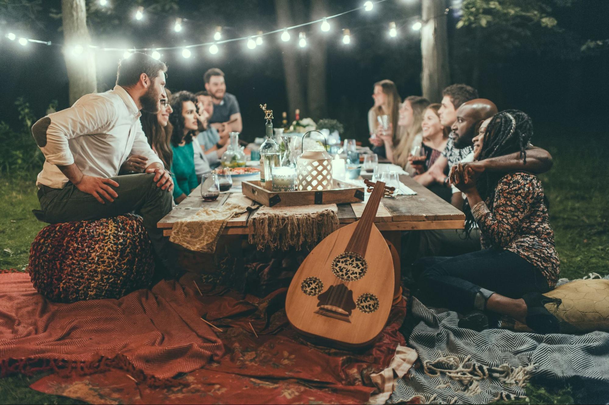 A group of friends enjoying a stylish, bohemian-themed dinner party outdoors at night, showcasing creative party hosting hacks.