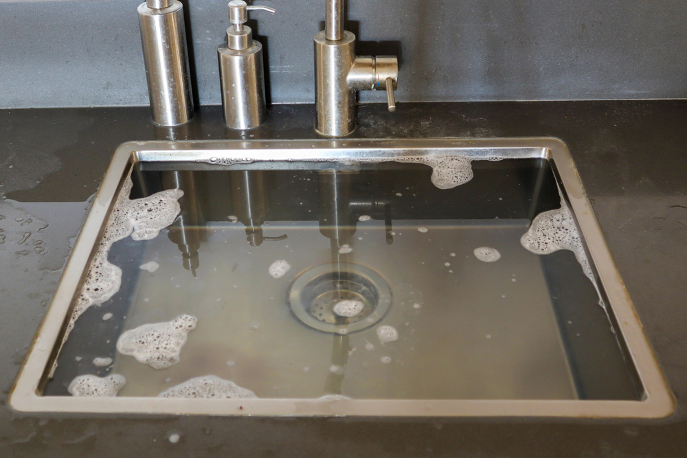 Blocked kitchen sink filled with cloudy standing water from a clogged drain.