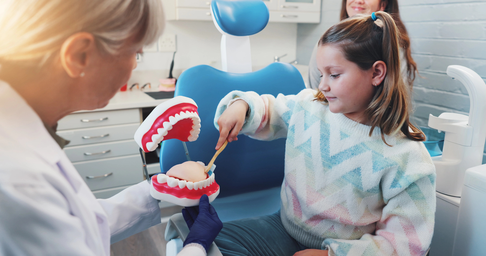 Friendly dentist teaching a child how to brush their teeth using a dental model