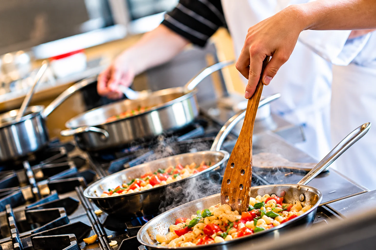 Italian cooking in a professional restaurant kitchen, with chefs preparing fresh pasta, tomatoes and herbs in steaming pans.