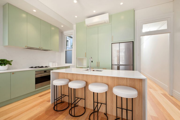 Refaced Manly kitchen with soft sage green cabinet doors, a white benchtop and timber-and-brass handles.