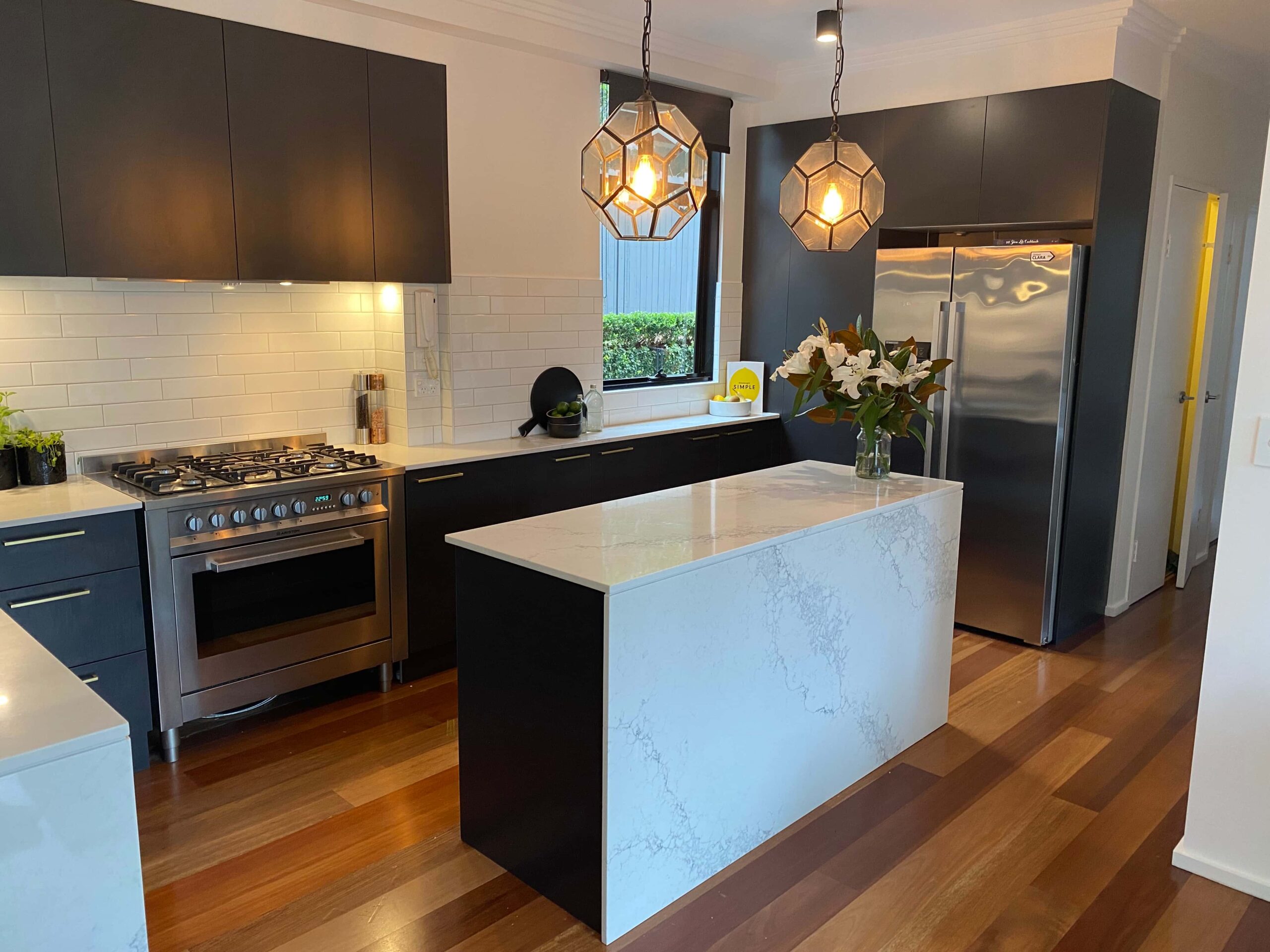 Modern kitchen renovation in the Northern Beaches with dark cabinets, white counters, and pendant lighting.