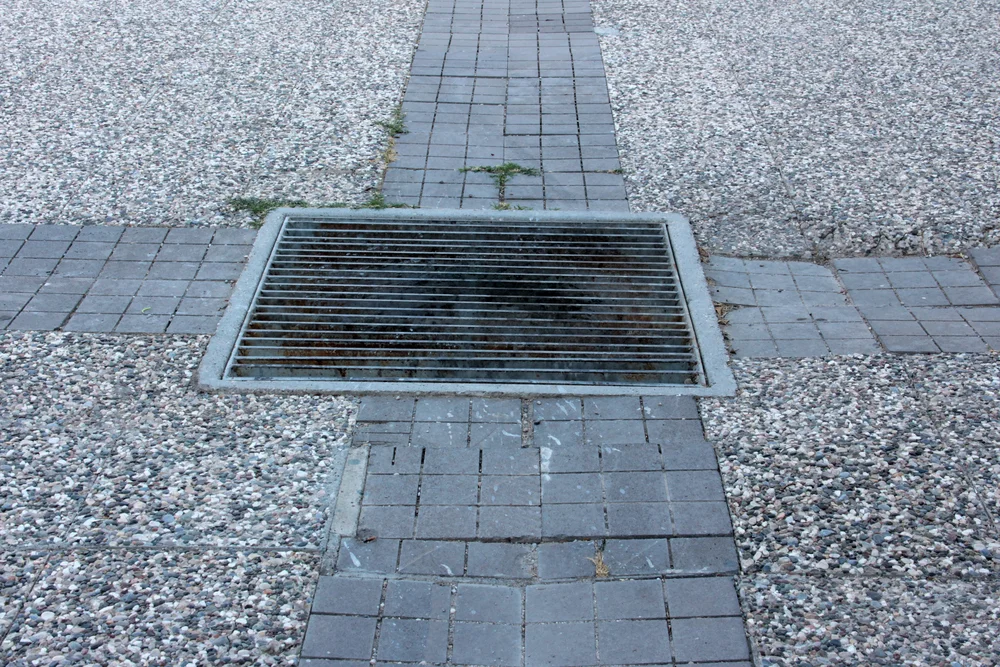 Outdoor stormwater drain grate surrounded by garden mulch and debris that can contribute to a blocked stormwater drain.