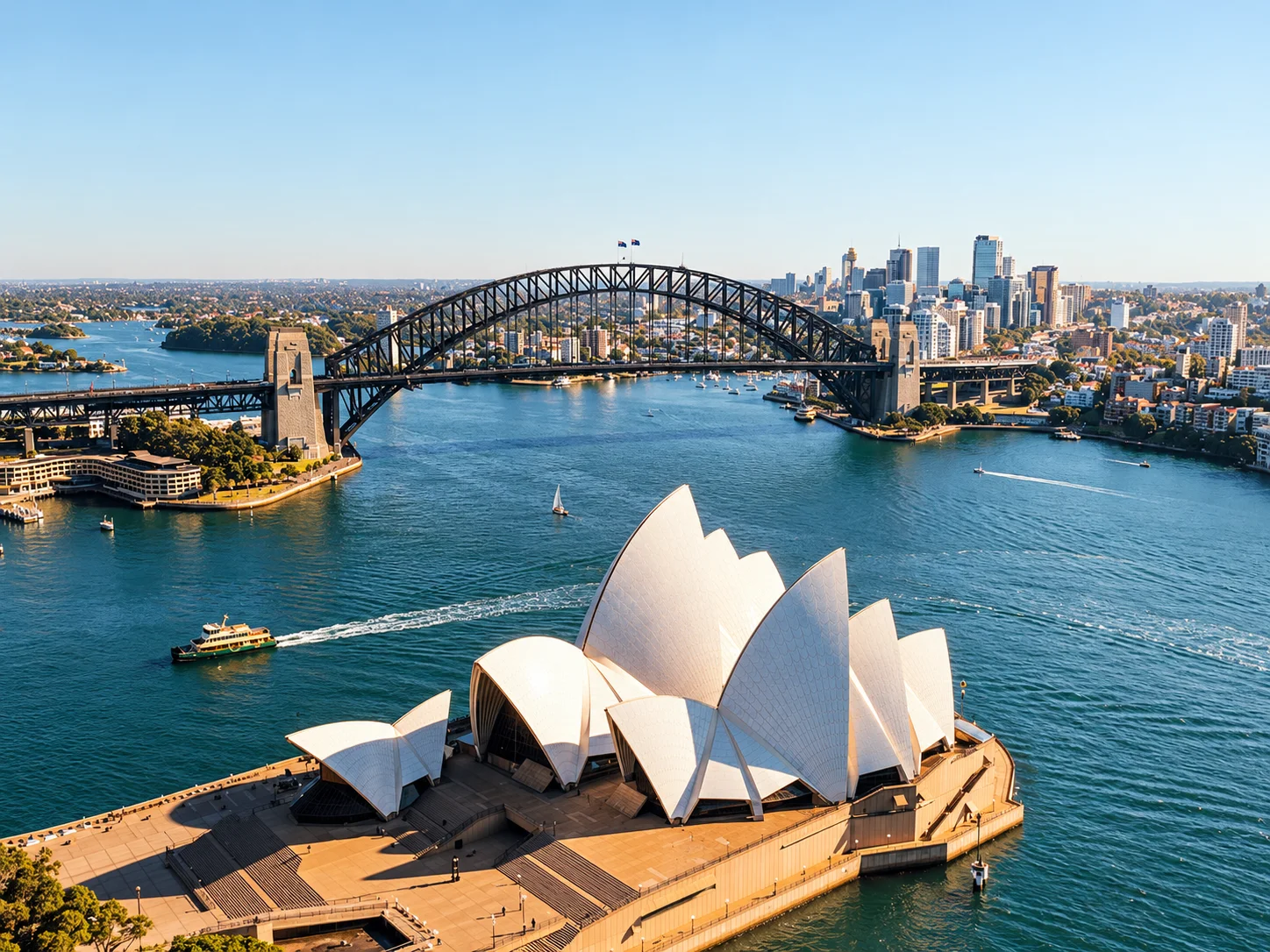 Aerial view of Sydney Opera House and Harbour Bridge overlooking Sydney Harbour on a sunny day.