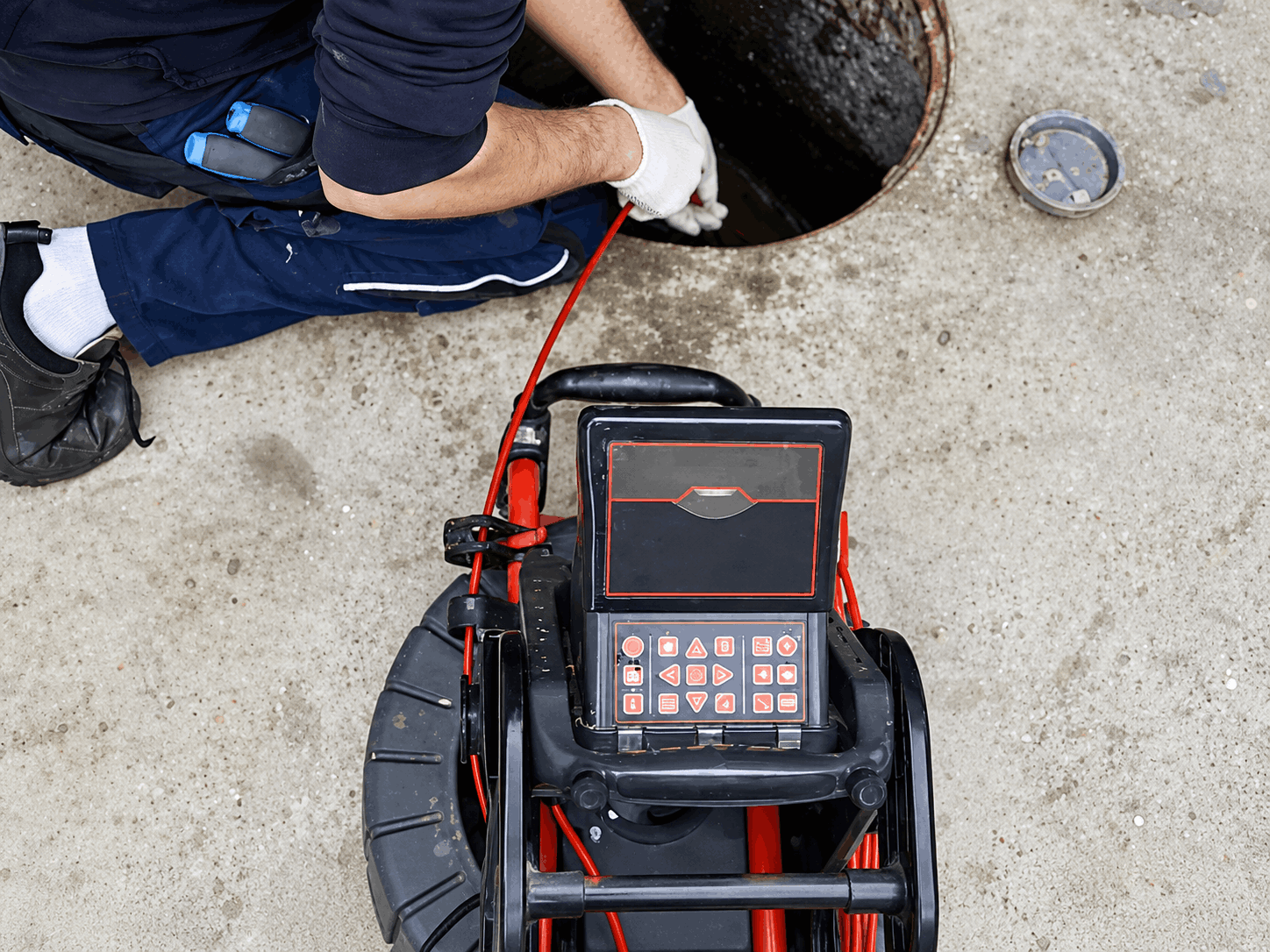A technician performs a Sydney plumbing cctv drain camera inspection, feeding a cable into a manhole while monitoring.
