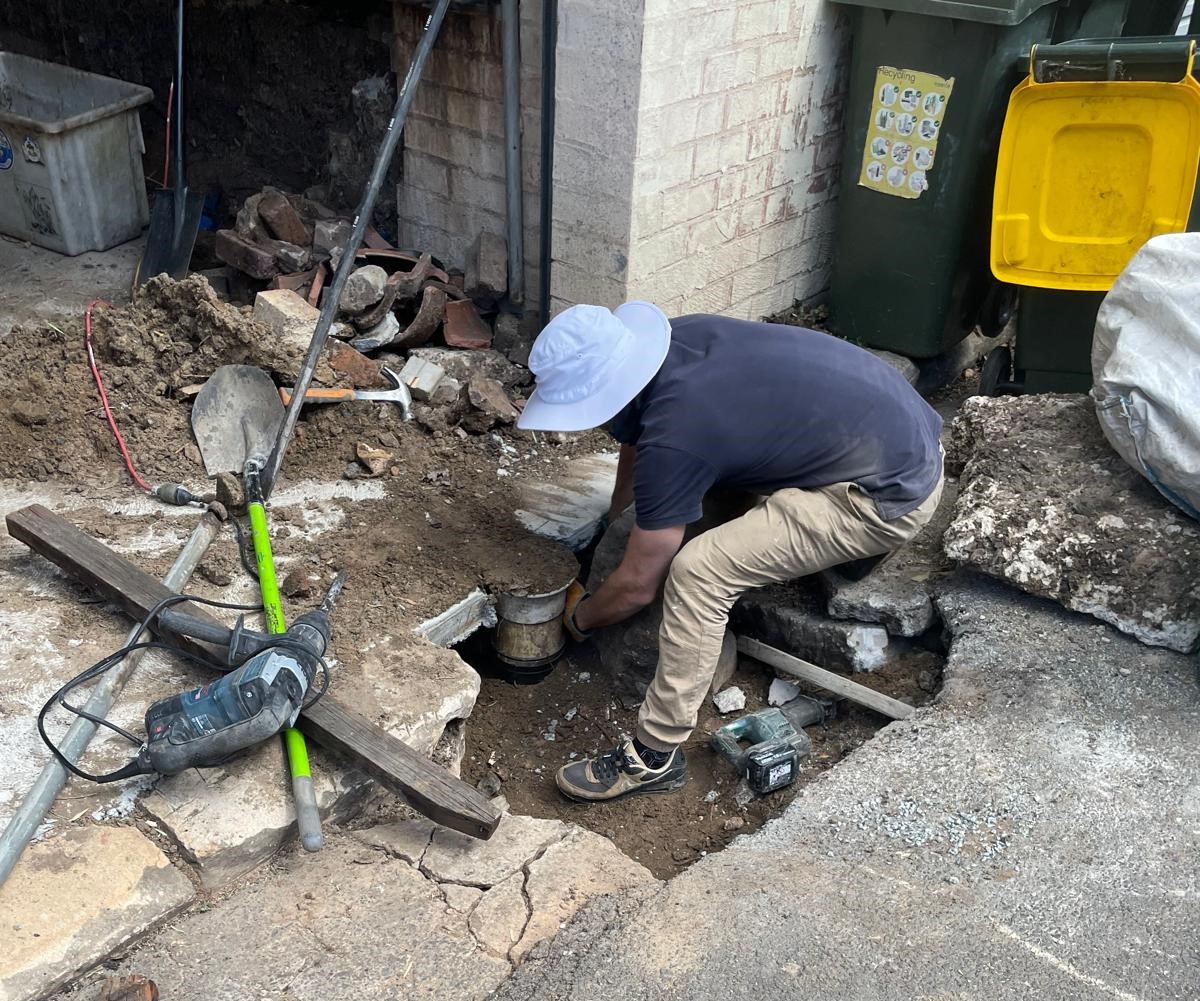 Plumber carrying out an underground drain pipe repair in an excavated area.