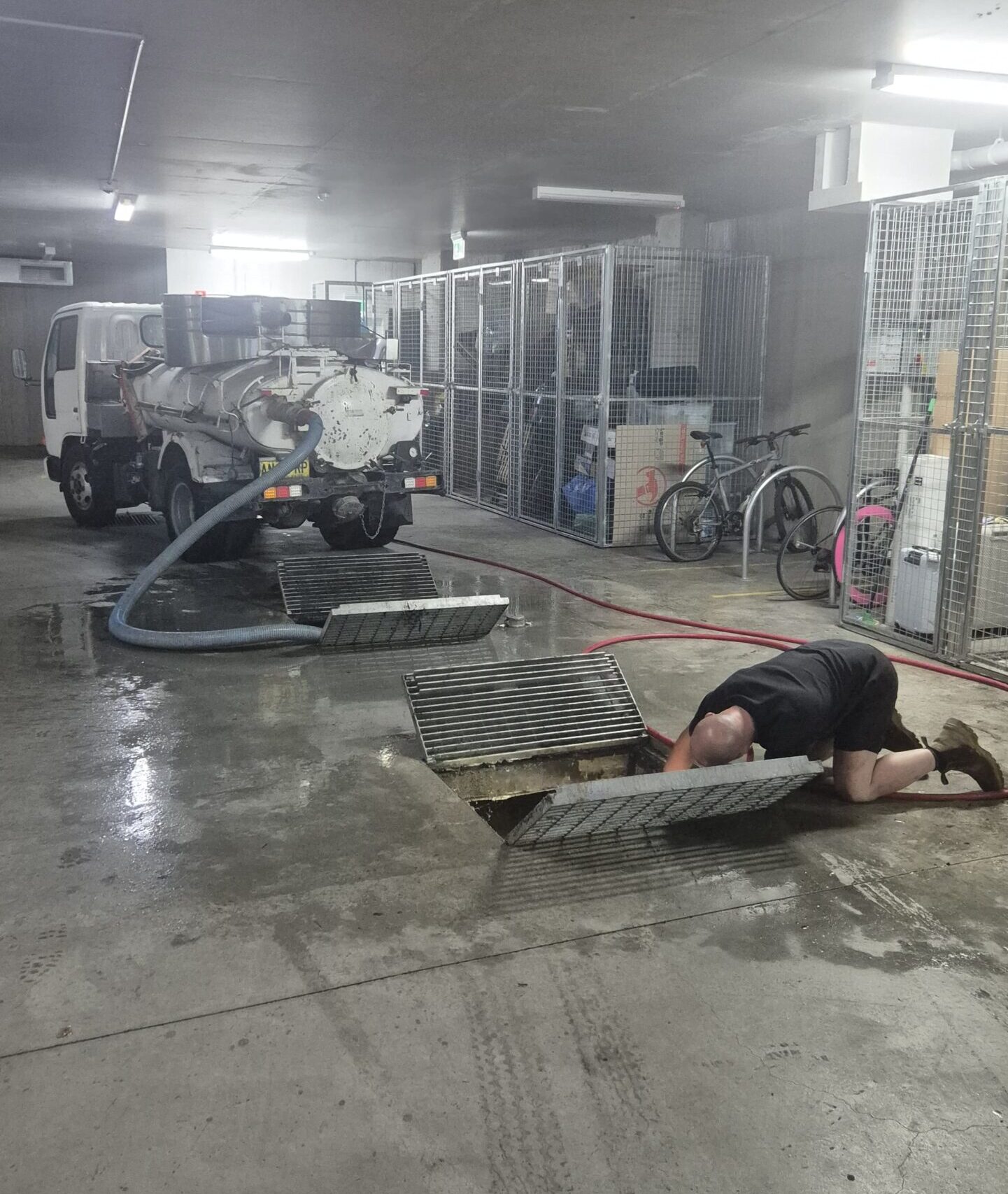UniPump technician working at an open pit in an underground car park, with a vacuum truck and hoses nearby.